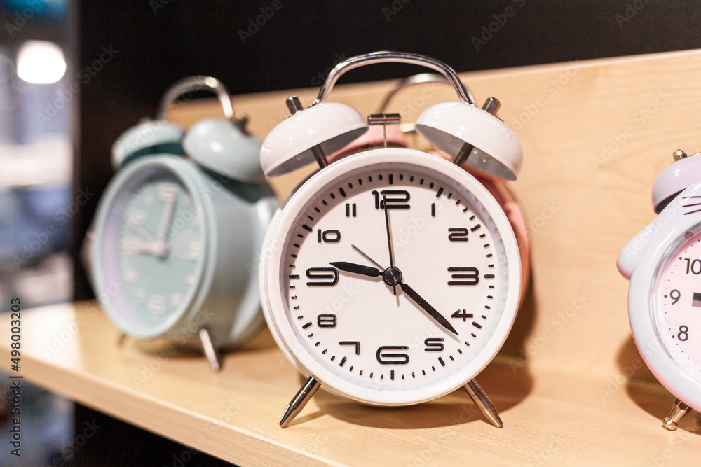 Round alarm clock on the store shelf close-up. Sale of various watches and alarm clocks of different colors. Retro alarm clock on the table, vintage tone. Round alarm clock on the store shelf close-up. Sale of various watches and alarm clocks of different colors. Retro alarm clock on the table, vintage tone.