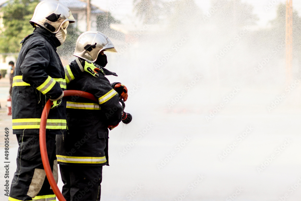 Fototapeta premium Firefighters using Twirl water fog type fire extinguisher to fighting with the fire flame from oil to control fire not to spreading out. Firefighter and industrial safety concept.