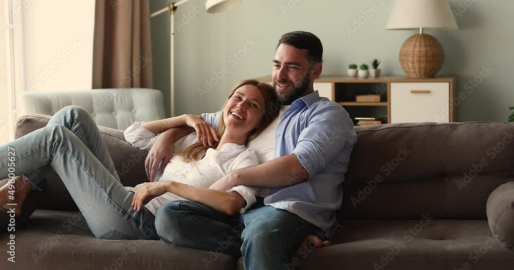Happy young 30s homeowners couple in love spend leisure at home, relaxing on sofa talking, enjoy carefree weekend. Spouses sit on couch daydreaming, planning vacation. Bank loan, relationship concept Happy young 30s homeowners couple in love spend leisure at home, relaxing on sofa talking, enjoy carefree weekend. Spouses sit on couch daydreaming, planning vacation. Bank loan, relationship concept