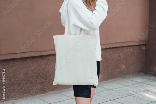 Woman holding white cotton bag on her shoulder, tote bag mockup.