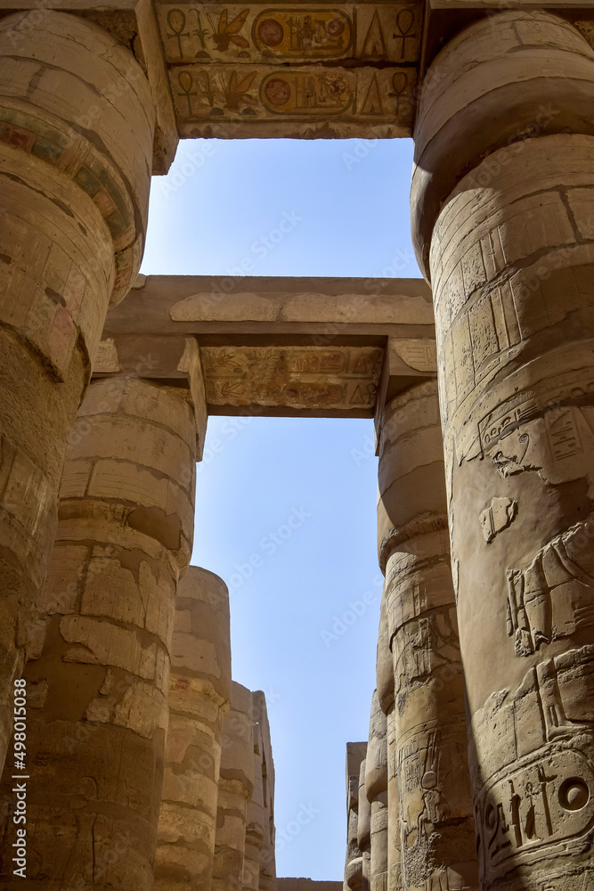 Ancient Egyptian hieroglyphs and symbols carved on columns of the complex of Karnak temple. Tall columns against blue sky. Great Hypostyle Hall at Temples of Karnak (ancient Thebes). Luxor, Egypt