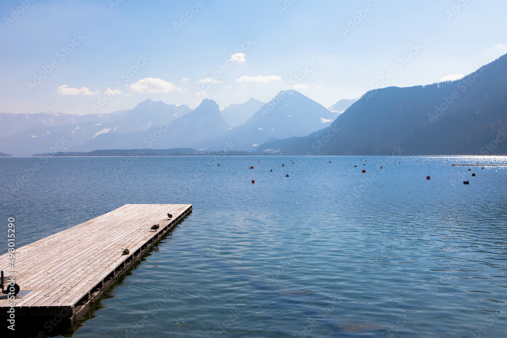 Panoramic view of an austrian lake with wooden pier and mountain range in the background. Salzkammergut, Upper Austria