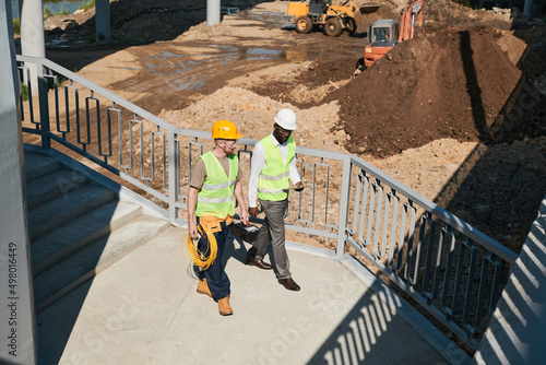 Two building contractors discussing project while standing at construction site, copy space