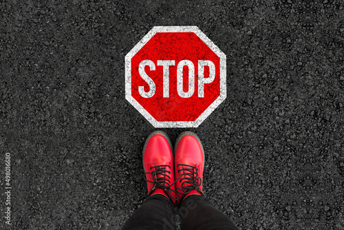 Canvas Print woman legs in boots standing on asphalt road and stop sign