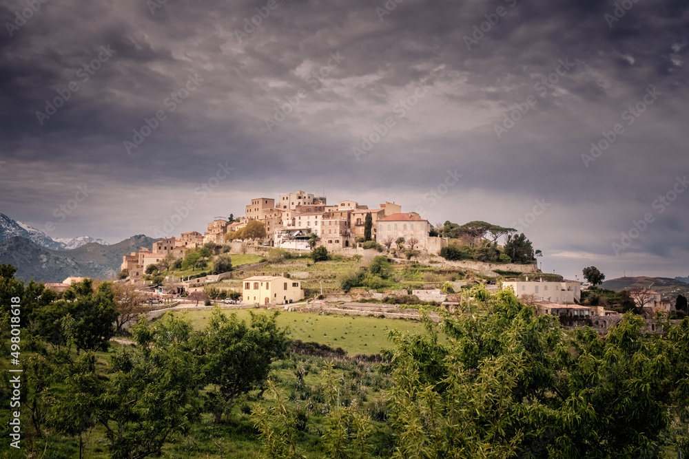 The hilltop village of Sant'Antonino in the Balagne region of Corsica with snow capped mountains in the distance
