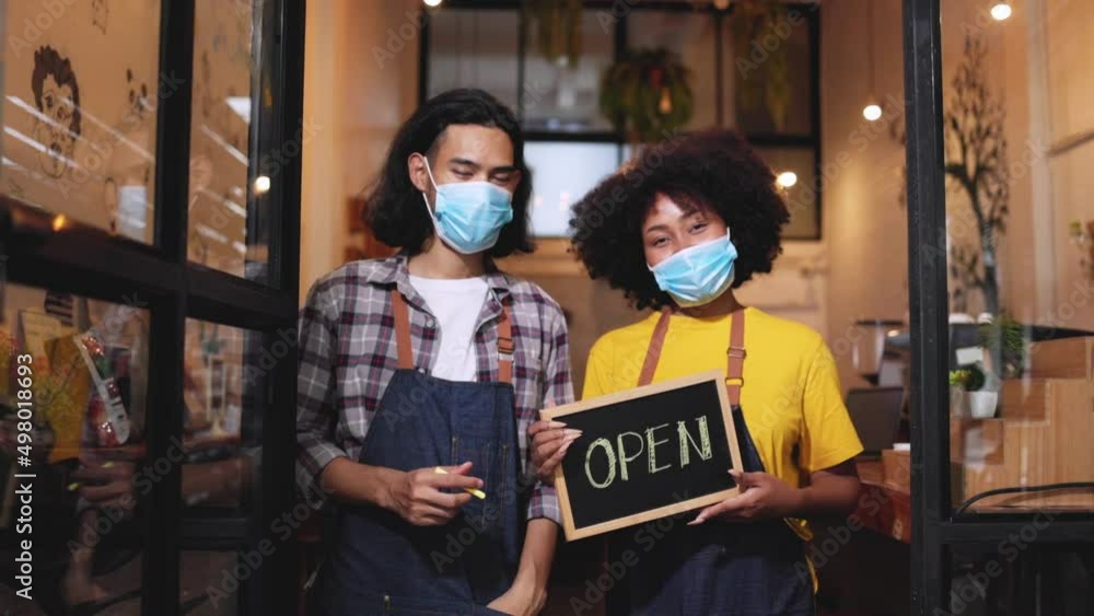 Young couple asian man and african woman manager in restaurant with digital tablet or notebookWoman coffee shop owner with face mask hold open sign .Small business concept. Young couple asian man and african woman manager in restaurant with digital tablet or notebookWoman coffee shop owner with face mask hold open sign .Small business concept.