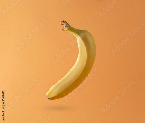 a yellow banana is hanging in the air on an orange background.
