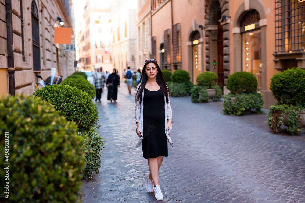 Young pretty woman in stylish fashion dress walking on street in Rome at sunny day. Vacation and female fashion city lifestyle concept