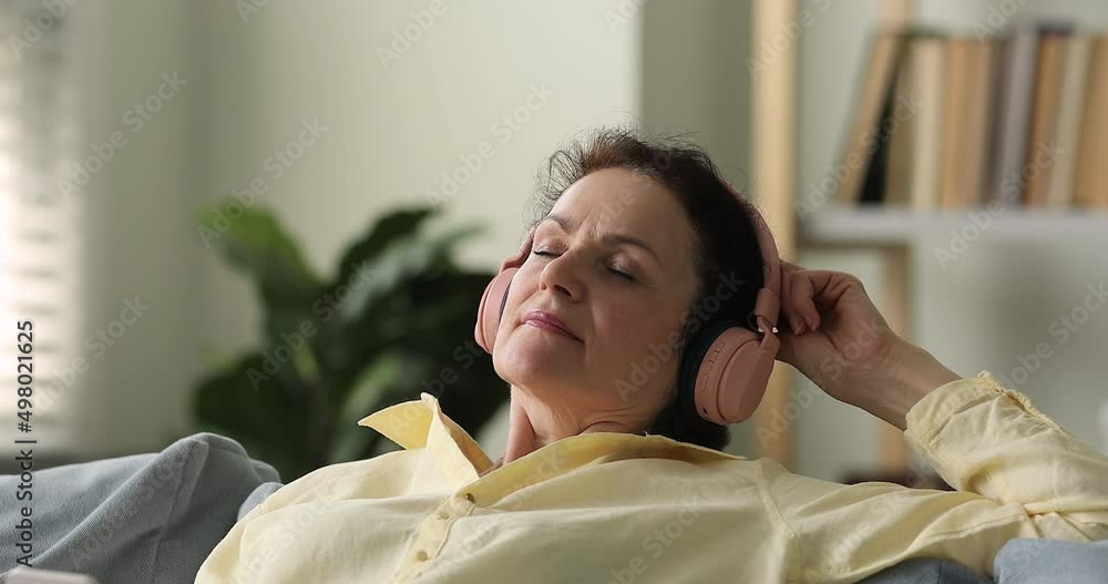 Peaceful mature lady wear wireless digital earphones relax on sofa at living room listen to audio book online. Happy tranquil older adult woman in headset rest with good music enjoy high sound quality Peaceful mature lady wear wireless digital earphones relax on sofa at living room listen to audio book online. Happy tranquil older adult woman in headset rest with good music enjoy high sound quality