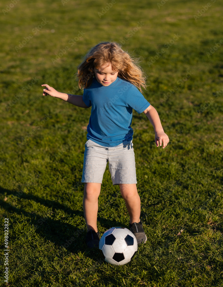 Obraz premium Soccer kid boy playing football. Child boy play football on outdoor field. Children score goal at soccer game. Kid kicking a football ball on a grass.