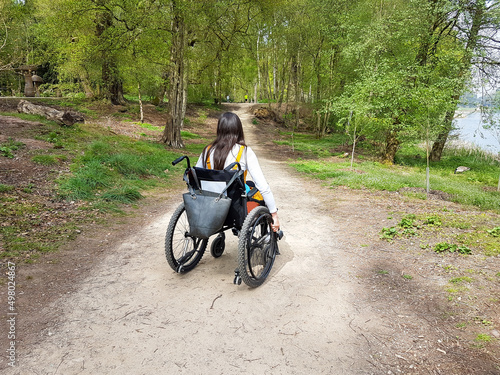 Young woman with long dark hair wheels herself along in her wheelchair enjoying the freedom the chair gives her to get out in the countryside despite her disability.