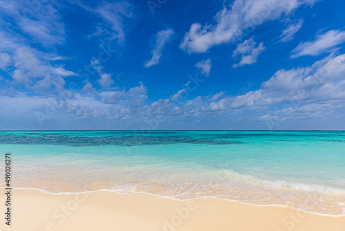 Closeup sandy beach waves and blue summer sky. Panoramic beach landscape. Empty tropical beach and seascape  horizon. Bright blue sky  soft sand  calmness  tranquil seaside relaxing sunlight  summer 