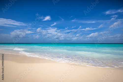 Closeup sandy beach waves and blue summer sky. Panoramic beach landscape. Empty tropical beach and seascape, horizon. Bright blue sky, soft sand, calmness, tranquil seaside relaxing sunlight, summer  photo