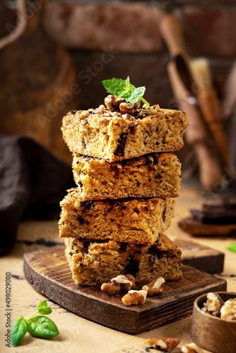 Pumpkin blondie bars with chocolate and walnuts close-up. Brownie pie slices on a serving wooden board on the dark culinary background. Baking for Thanksgiving	