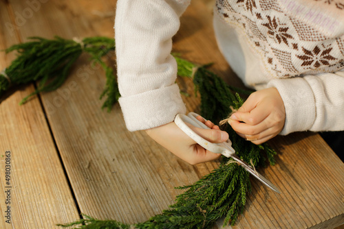 girl making cedar wreath on wooden craft table. child cutting a sisal thread.