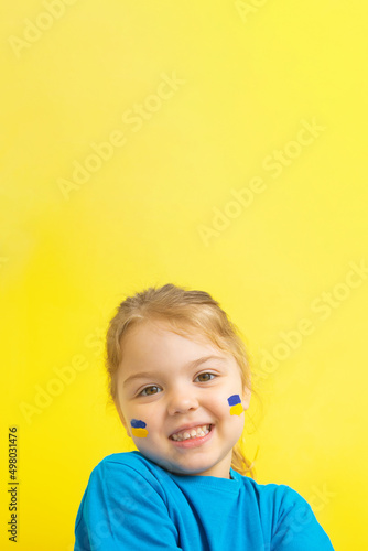 A girl with a painted Ukrainian flag of yellow and blue on her cheeks. Vertical photo with copy space