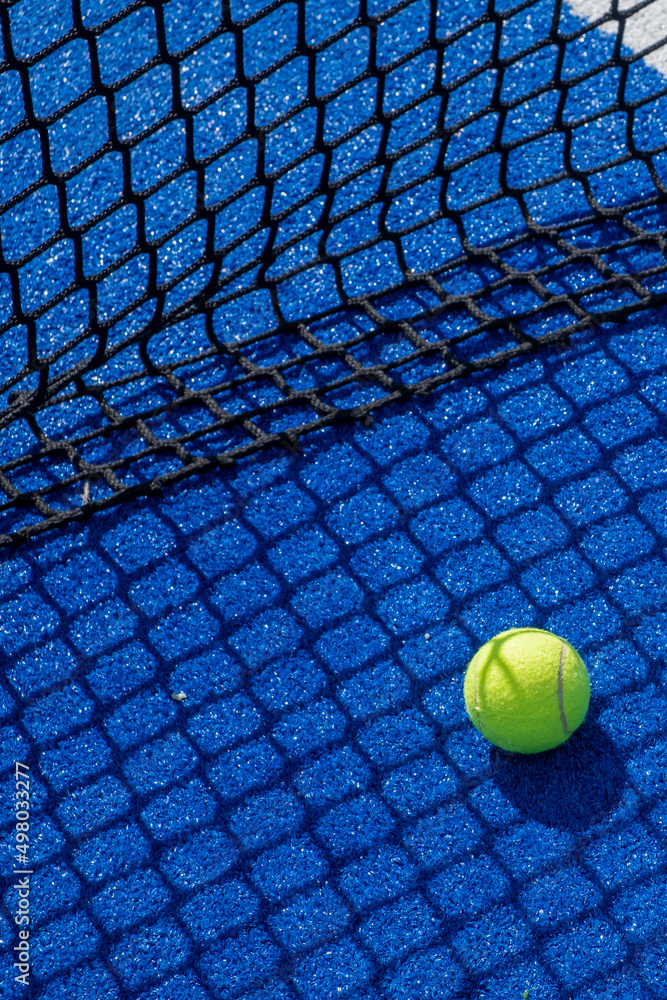 paddle tennis ball in the shade of the net of a blue paddle tennis court