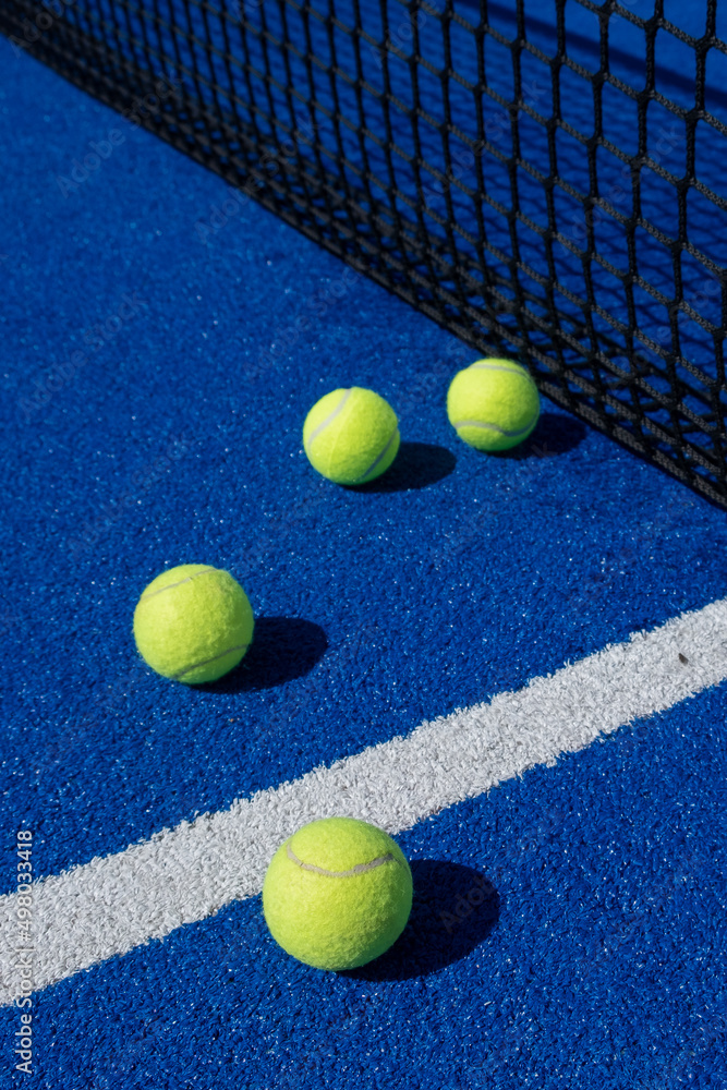 four balls next to the net and the center line of a blue paddle tennis court