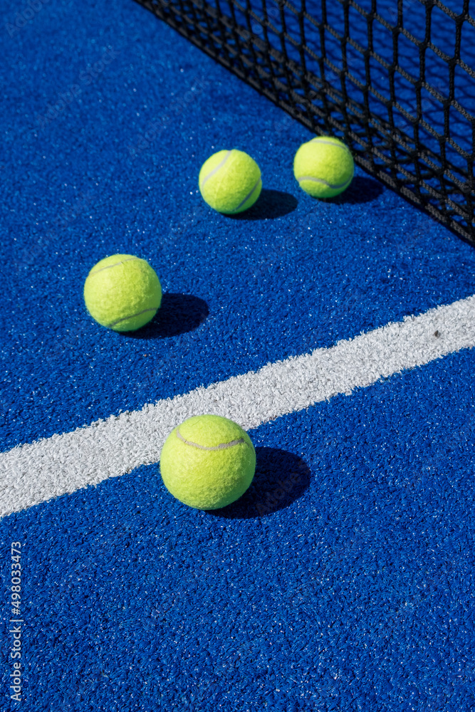four balls next to the net and the center line of a blue paddle tennis court