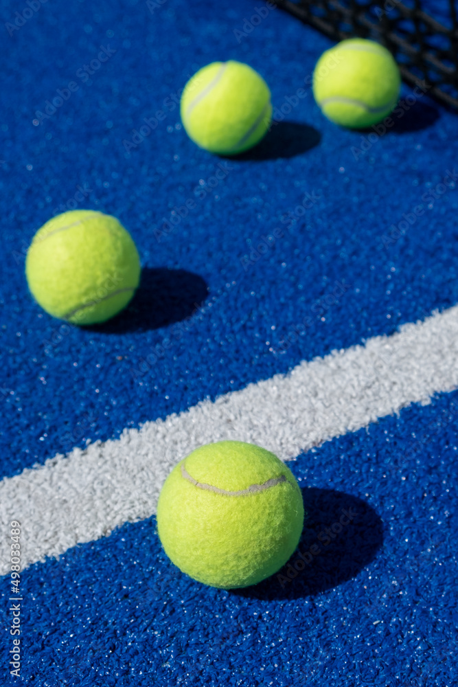 four balls next to the net and the center line of a blue paddle tennis court