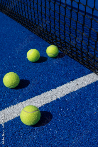 four balls next to the net and the center line of a blue paddle tennis court © Vic