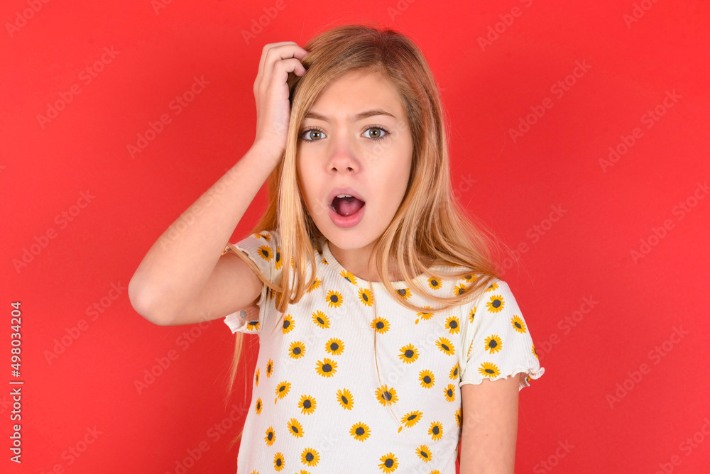 Embarrassed blonde little kid girl wearing daisy t-shirt red over background with shocked expression, expresses great amazement, Puzzled model poses indoor Embarrassed blonde little kid girl wearing daisy t-shirt red over background with shocked expression, expresses great amazement, Puzzled model poses indoor