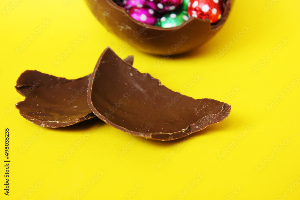 A cracked chocolate Easter egg with colorful little round candies inside. Happy Easter. Chocolate. Sweets for children and adults. Candy. Dessert. Copy space. Top view. Flat lay A cracked chocolate Easter egg with colorful little round candies inside. Happy Easter. Chocolate. Sweets for children and adults. Candy. Dessert. Copy space. Top view. Flat lay