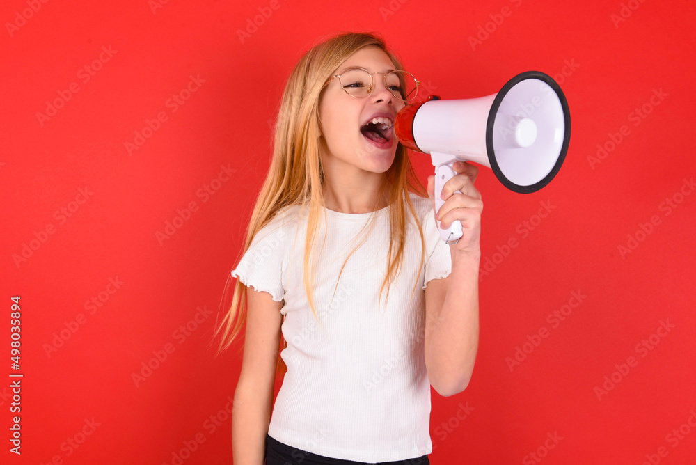 blonde little kid girl wearing white t-shirt over red background Through Megaphone with Available Copy Space blonde little kid girl wearing white t-shirt over red background Through Megaphone with Available Copy Space