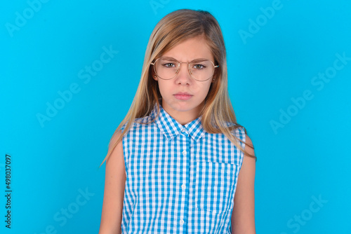 Obraz na plátně little kid girl with glasses wearing plaid shirt over blue background  frowning his eyebrows being displeased with something