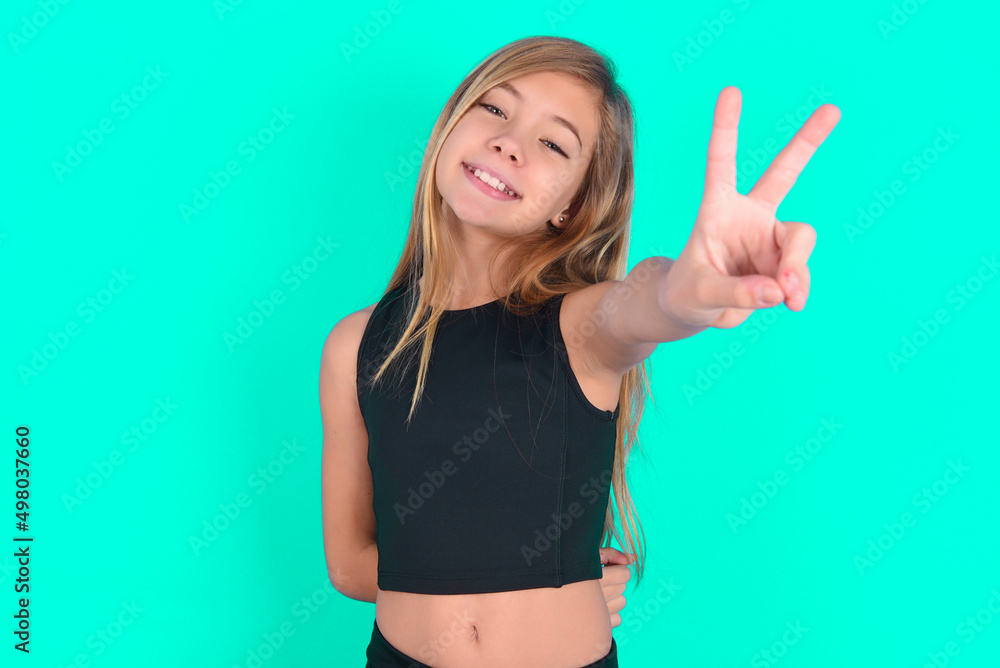 Fototapeta premium blonde little kid girl wearing black sport clothes over green background directs fingers at camera selects someone. I recommend you. Best choice