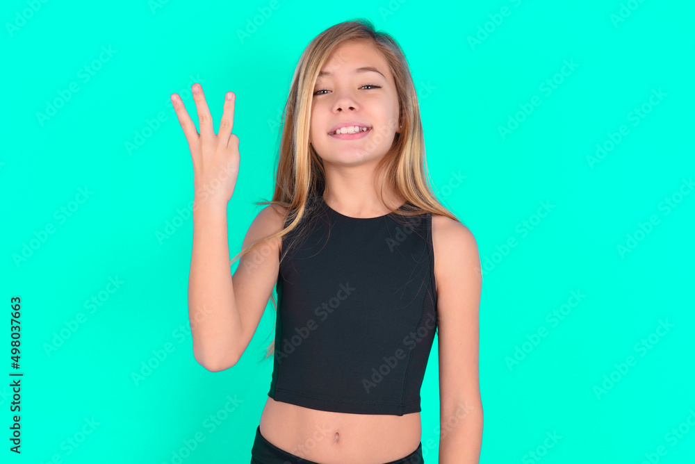 blonde little kid girl wearing black sport clothes over green background smiling and looking friendly, showing number three or third with hand forward, counting down blonde little kid girl wearing black sport clothes over green background smiling and looking friendly, showing number three or third with hand forward, counting down