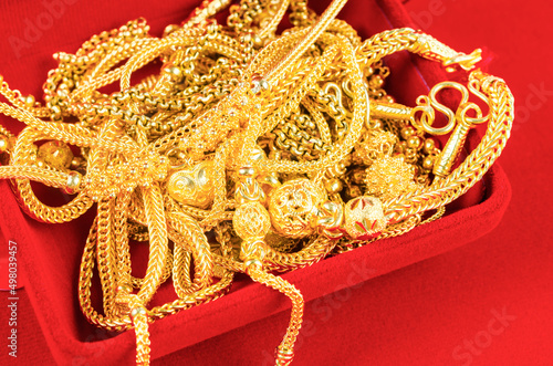 Many gold necklaces in a red velvet box on red background.