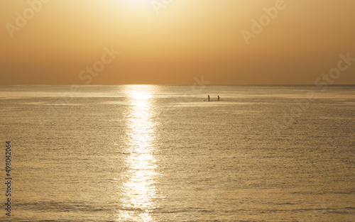Silhouettes of man and woman kayaking in the sea at sunrise. © Telly