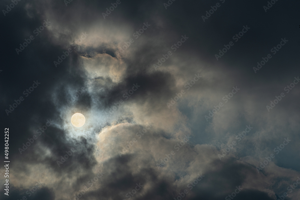 Obraz premium Photograph of full Moon between heavy clouds. Dark cloudy gloomy sky.