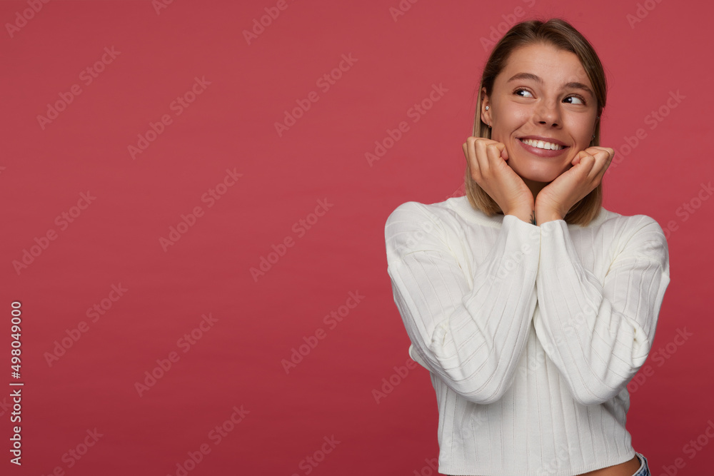 indoor portrait of young female posing over red background looks aside and smiles broadly indoor portrait of young female posing over red background looks aside and smiles broadly