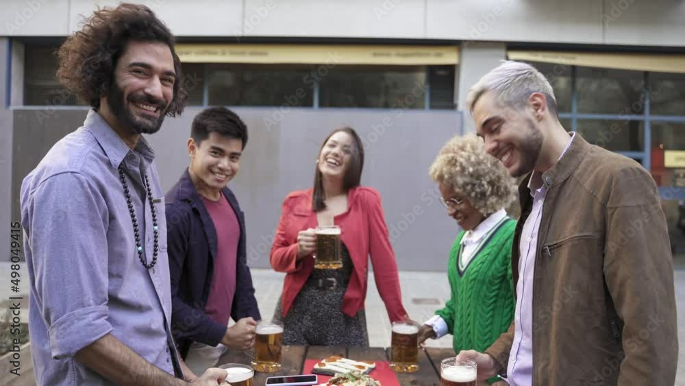 Happy multiracial friends toasting beer in a celebration looking to camera Happy multiracial friends toasting beer in a celebration looking to camera