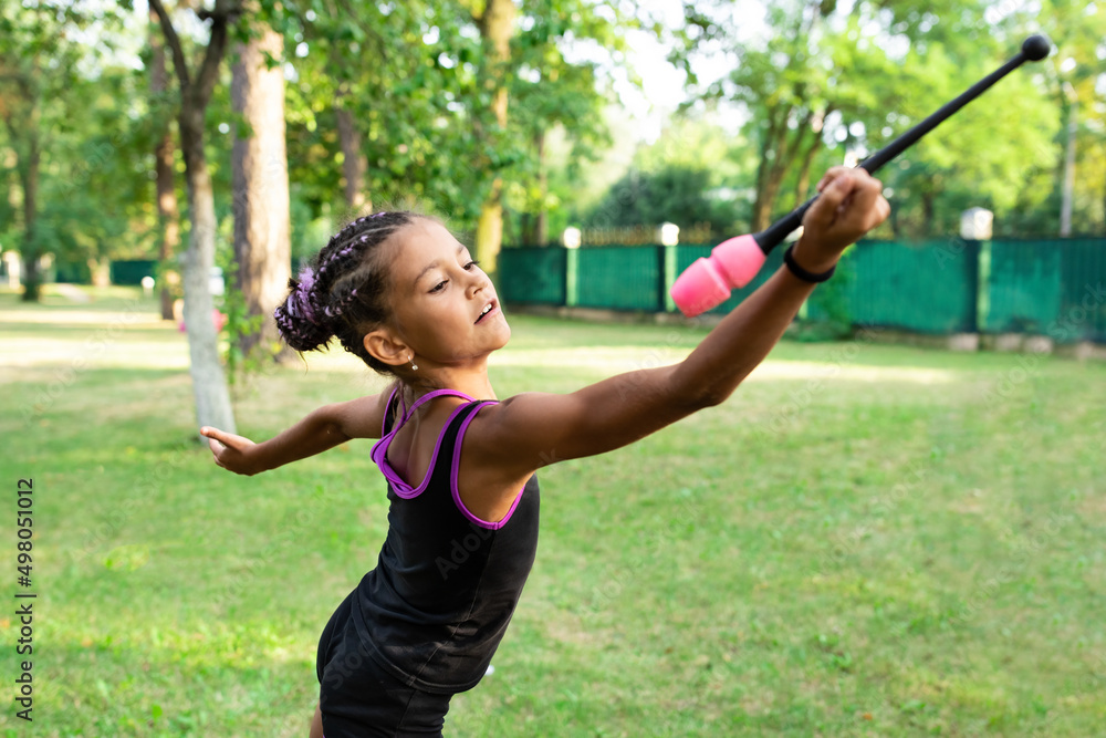 Girl doing exercise with clubs on rhythmic gymnastics training outdoors in summer in sports camp Girl doing exercise with clubs on rhythmic gymnastics training outdoors in summer in sports camp