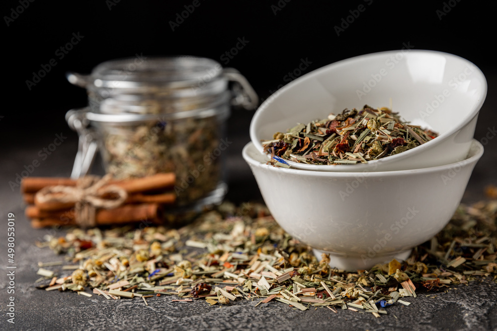 Herbal tea in a ceramic bowl and a glass jar on a black textural background. Detox and immunity tea. Herbal collection of chamomile, mint, lemon balm. rosehip and dried fruit pieces. Herbal tea in a ceramic bowl and a glass jar on a black textural background. Detox and immunity tea. Herbal collection of chamomile, mint, lemon balm. rosehip and dried fruit pieces.