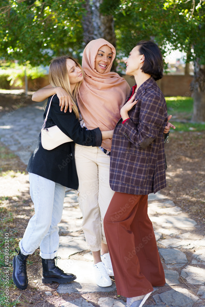 Delighted young diverse women embracing and smiling in park