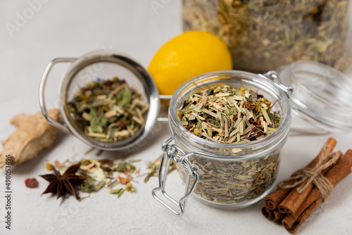 Aromatic herbal tea in a glass jar on a light gray background. Tea set with lemon, cinnamon, ginger and anise. Immune and vitamin tea. Cold drink. 