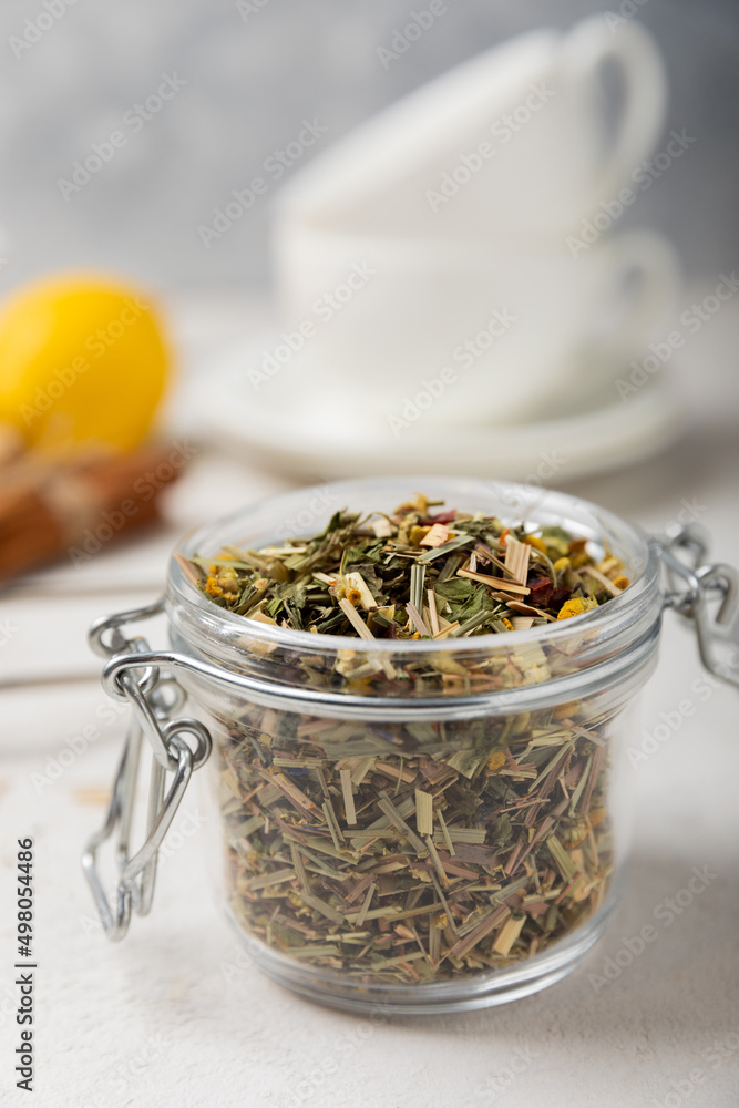 Fototapeta premium Aromatic herbal tea in a glass jar on a light gray background. Tea set with lemon, cinnamon, ginger and anise. Immune and vitamin tea. Cold drink. side view.