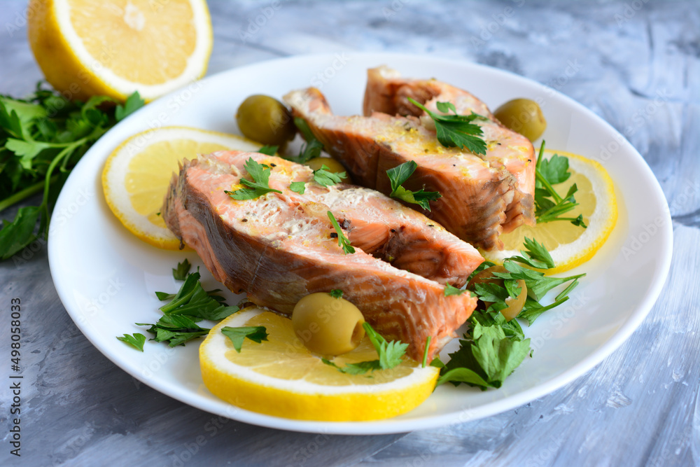 roasted salmon steaks on plate with lemon slices, green olives and parsley, close-up roasted salmon steaks on plate with lemon slices, green olives and parsley, close-up