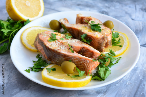 roasted salmon steaks on plate with lemon slices, green olives and parsley, close-up