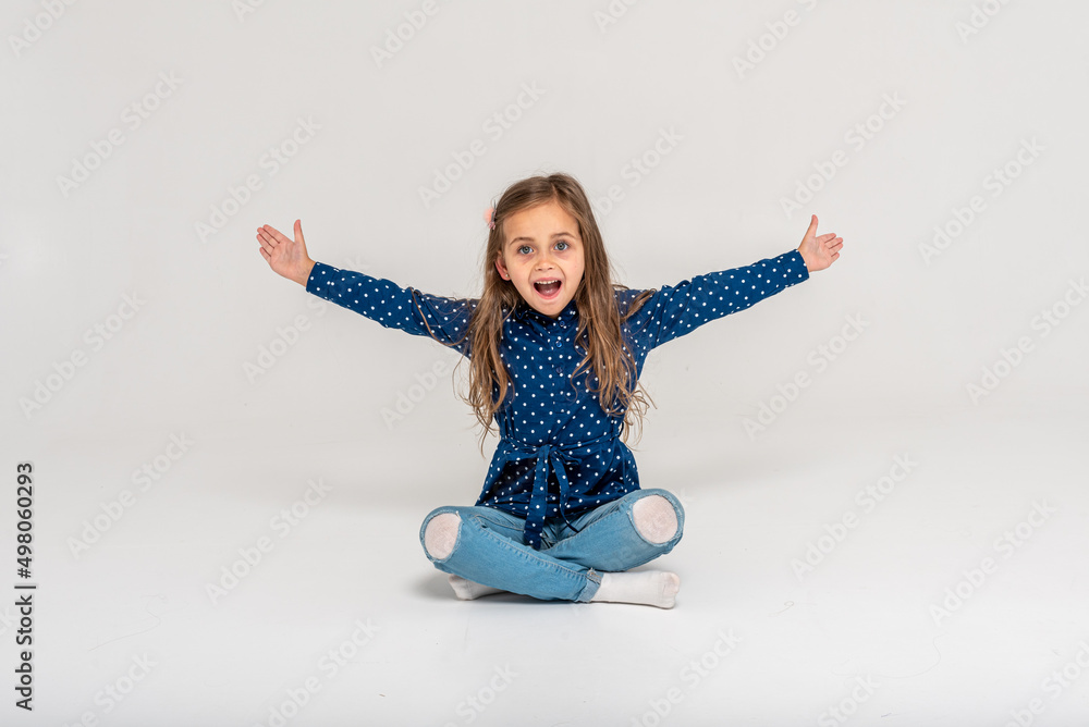 little beautiful, emotional, girl shouting, raised her hands sitting on the floor on a white background looking straight