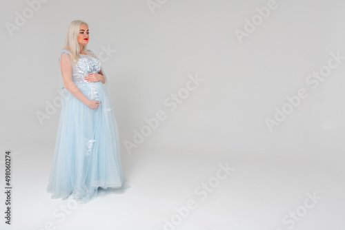 Young pregnant woman  mom in a light dress  on a white background  indoors. Place for inscription 