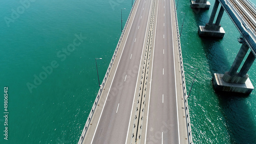 Flight above new white bridge with moving vehicles. Action. Breathtaking marine landscape with a long bridge above blue calm water.