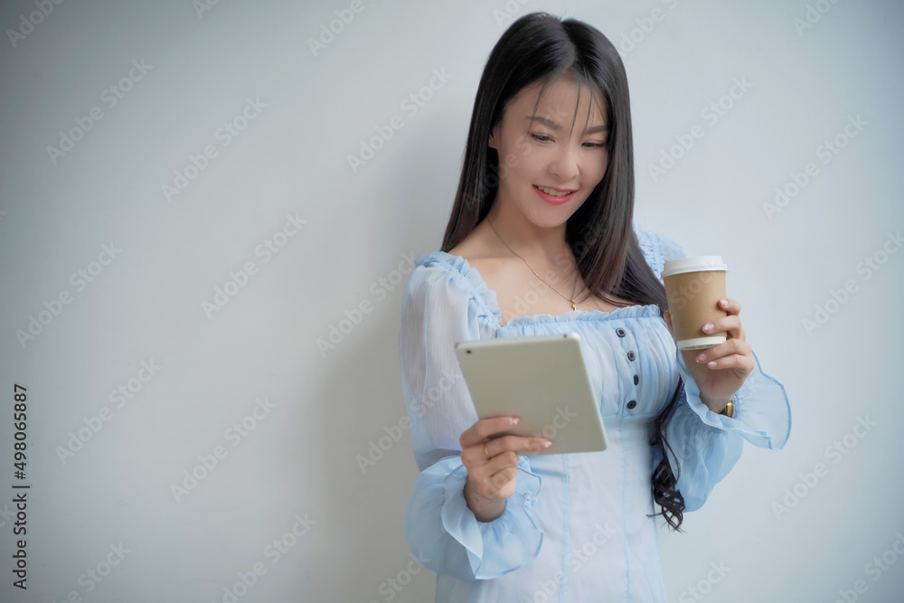 Businesswoman standing in office, drinking coffee and analyzing profits. Market trends with tablets, business ideas in Asia Businesswoman standing in office, drinking coffee and analyzing profits. Market trends with tablets, business ideas in Asia