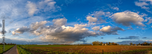 Eine Gewitterwolke in einem dramatischen Wolkenhimmel im Abendlicht der Sonne zieht mit ihren Wolkenfetzen über landwirtschaftlich genutztes Land