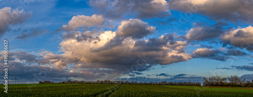 Eine Gewitterwolke in einem dramatischen Wolkenhimmel im Abendlicht der Sonne zieht mit ihren Wolkenfetzen über landwirtschaftlich genutztes Land