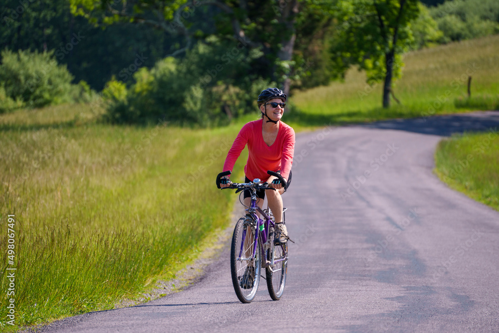 Happy woman wearing bike helmet looking aside biking on a country road on a spring summer day. Happy woman wearing bike helmet looking aside biking on a country road on a spring summer day.